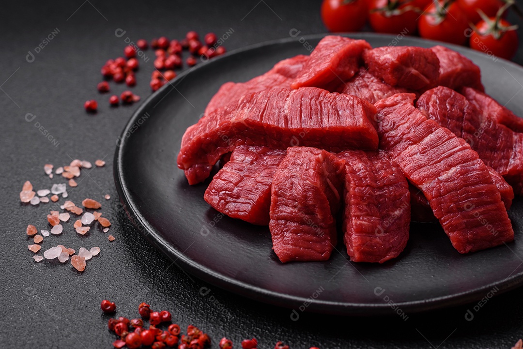 Fatias frescas e suculentas de carne crua com sal e especiarias sobre um fundo escuro de concreto