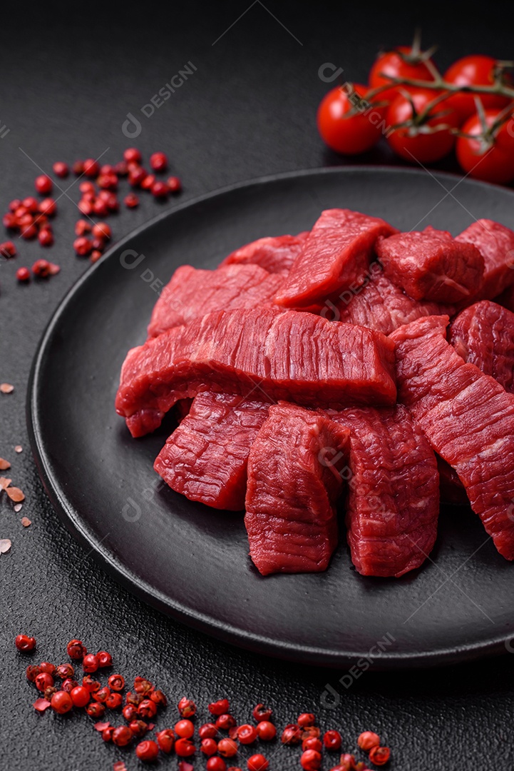 Fatias frescas e suculentas de carne crua com sal e especiarias sobre um fundo escuro de concreto