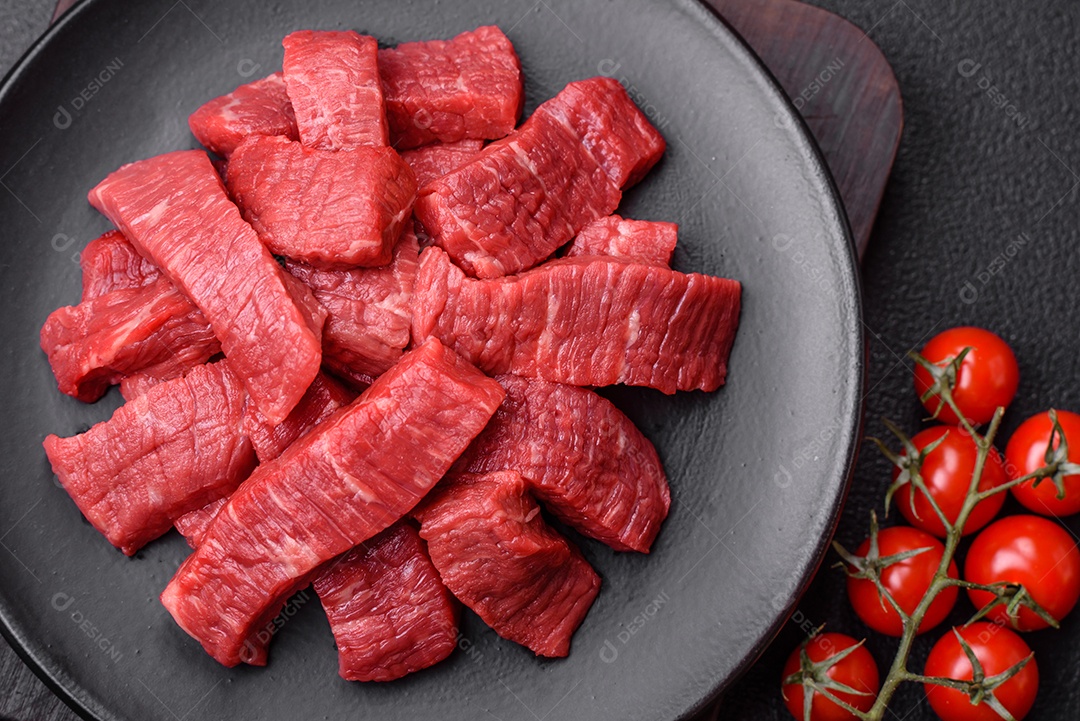 Fatias frescas e suculentas de carne crua com sal e especiarias sobre um fundo escuro de concreto