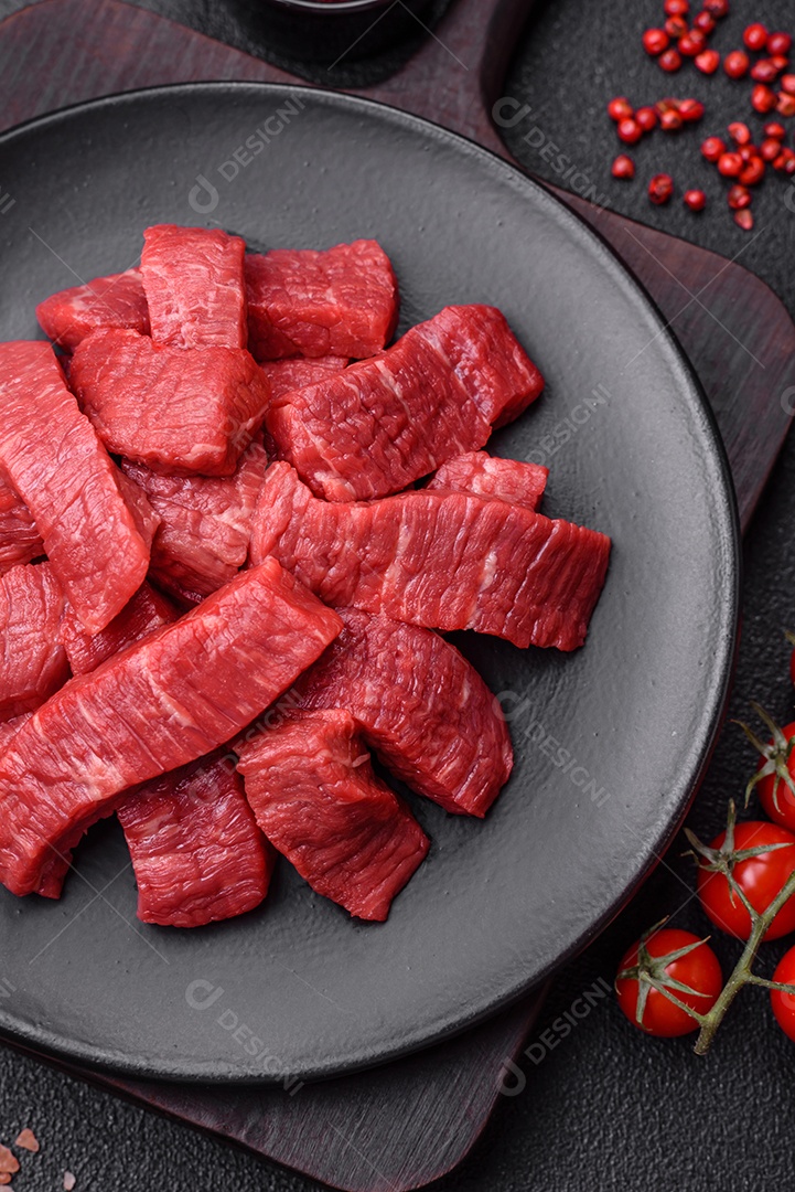 Fatias frescas e suculentas de carne crua com sal e especiarias sobre um fundo escuro de concreto