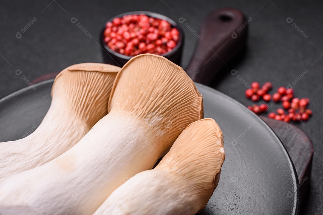 Cogumelos Pleurotus eryngii sobre um fundo escuro de concreto. Cogumelos comestíveis inteiros crus