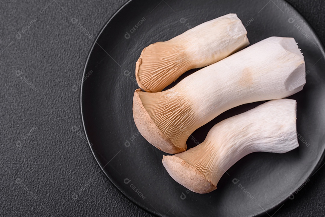 Cogumelos Pleurotus eryngii sobre um fundo escuro de concreto. Cogumelos comestíveis inteiros crus