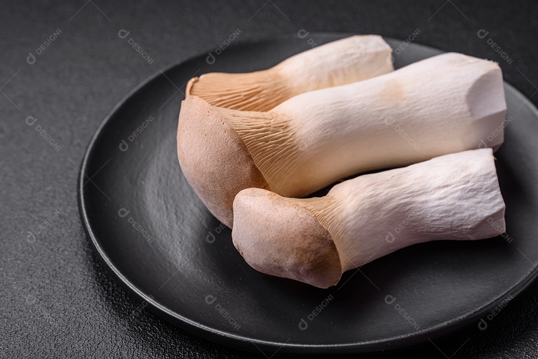 Cogumelos Pleurotus eryngii sobre um fundo escuro de concreto. Cogumelos comestíveis inteiros crus