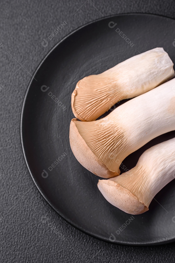 Cogumelos Pleurotus eryngii sobre um fundo escuro de concreto. Cogumelos comestíveis inteiros crus