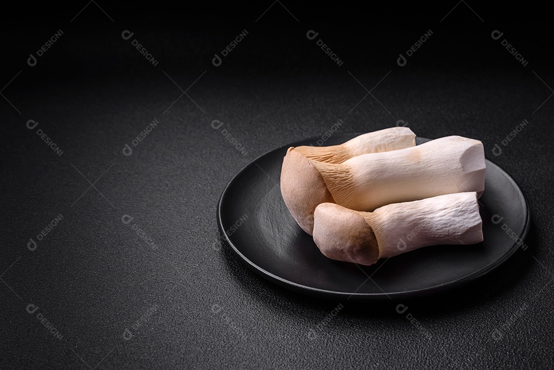 Cogumelos Pleurotus eryngii sobre um fundo escuro de concreto. Cogumelos comestíveis inteiros crus