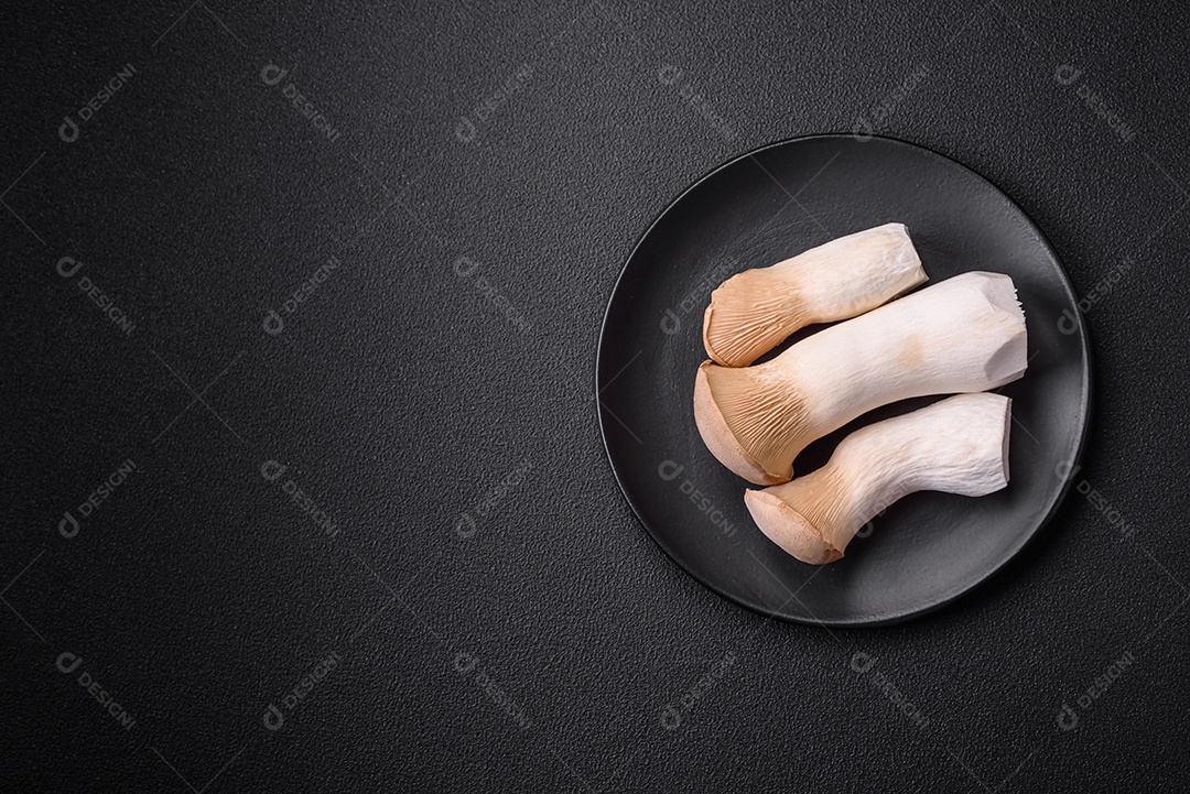 Cogumelos Pleurotus eryngii sobre um fundo escuro de concreto. Cogumelos comestíveis inteiros crus