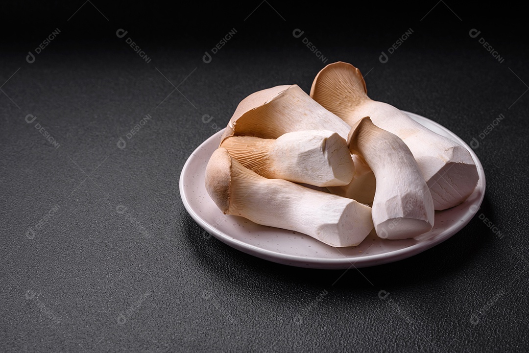 Cogumelos Pleurotus eryngii sobre um fundo escuro de concreto. Cogumelos comestíveis inteiros crus