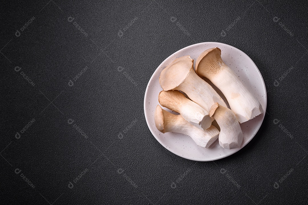 Cogumelos Pleurotus eryngii sobre um fundo escuro de concreto. Cogumelos comestíveis inteiros crus