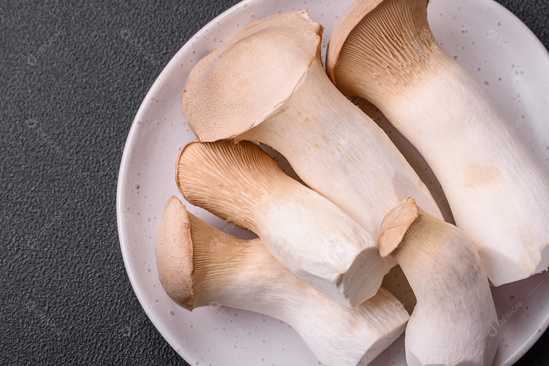Cogumelos Pleurotus eryngii sobre um fundo escuro de concreto. Cogumelos comestíveis inteiros crus