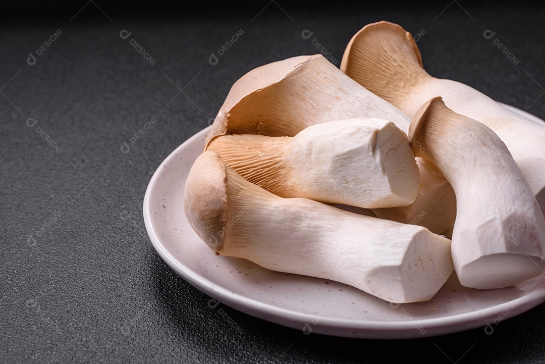 Cogumelos Pleurotus eryngii sobre um fundo escuro de concreto. Cogumelos comestíveis inteiros crus