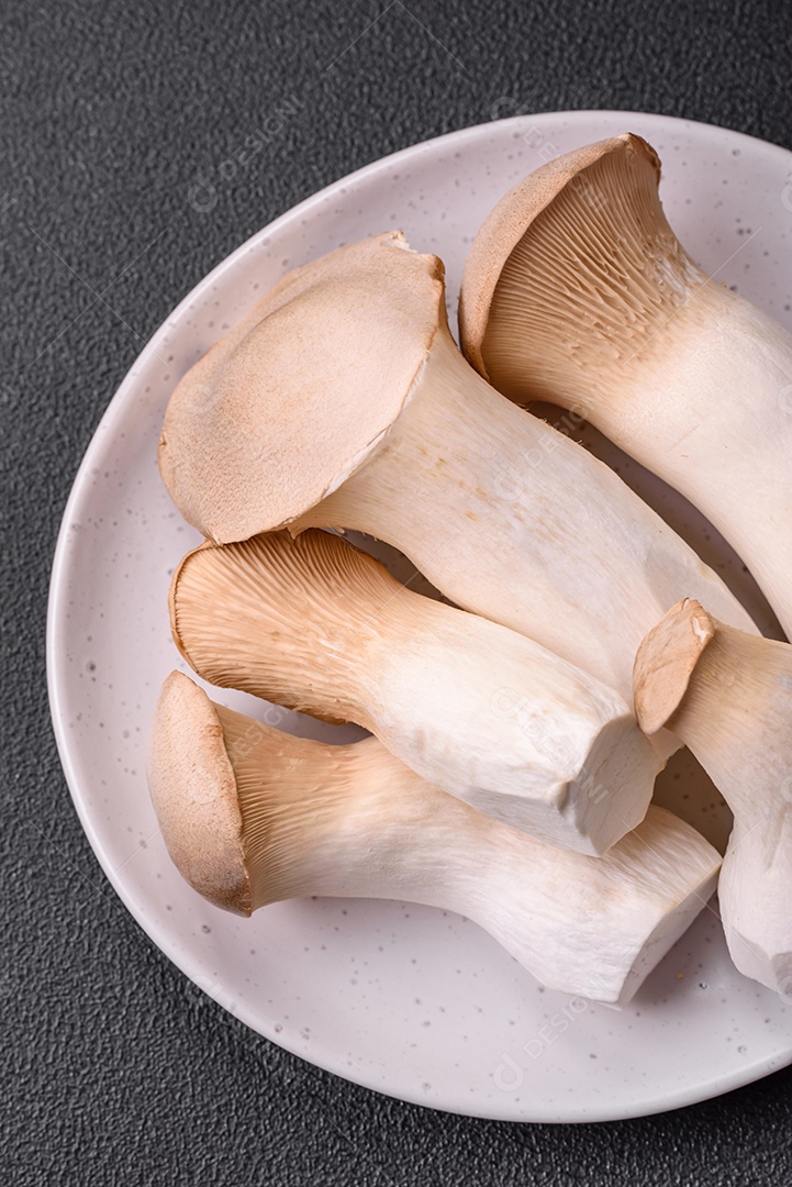 Cogumelos Pleurotus eryngii sobre um fundo escuro de concreto. Cogumelos comestíveis inteiros crus