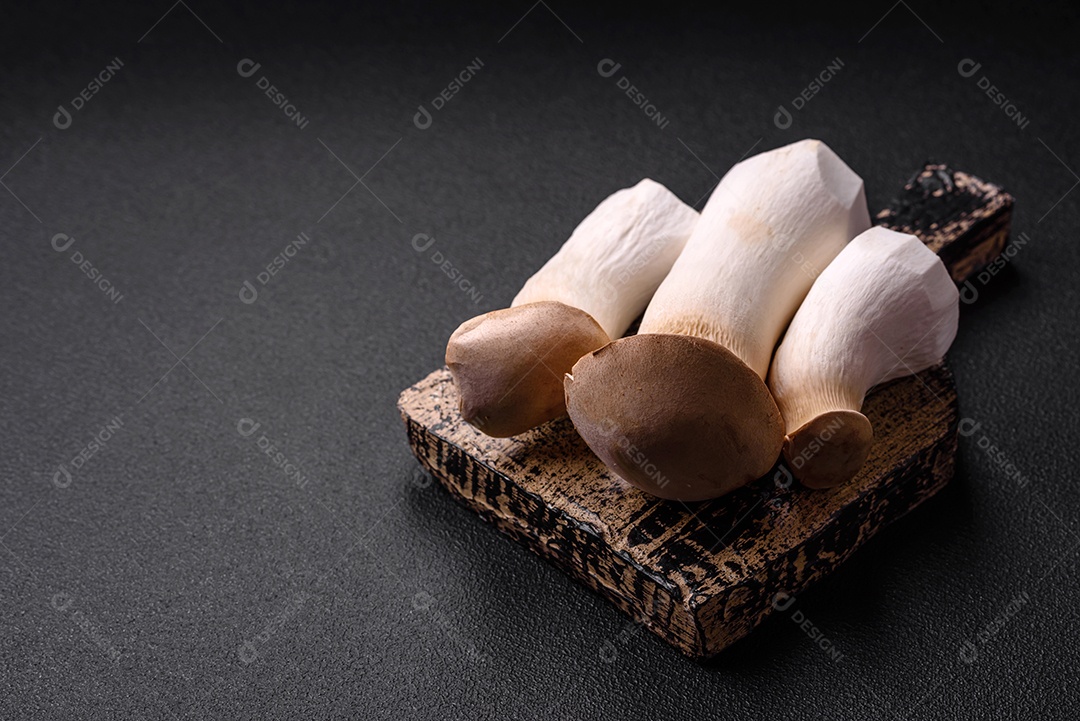 Cogumelos Pleurotus eryngii sobre um fundo escuro de concreto. Cogumelos comestíveis inteiros crus