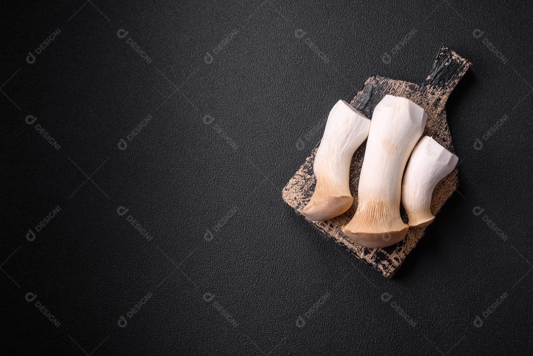 Cogumelos Pleurotus eryngii sobre um fundo escuro de concreto. Cogumelos comestíveis inteiros crus