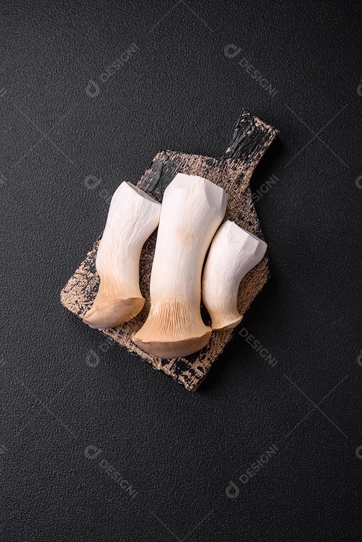 Cogumelos Pleurotus eryngii sobre um fundo escuro de concreto. Cogumelos comestíveis inteiros crus