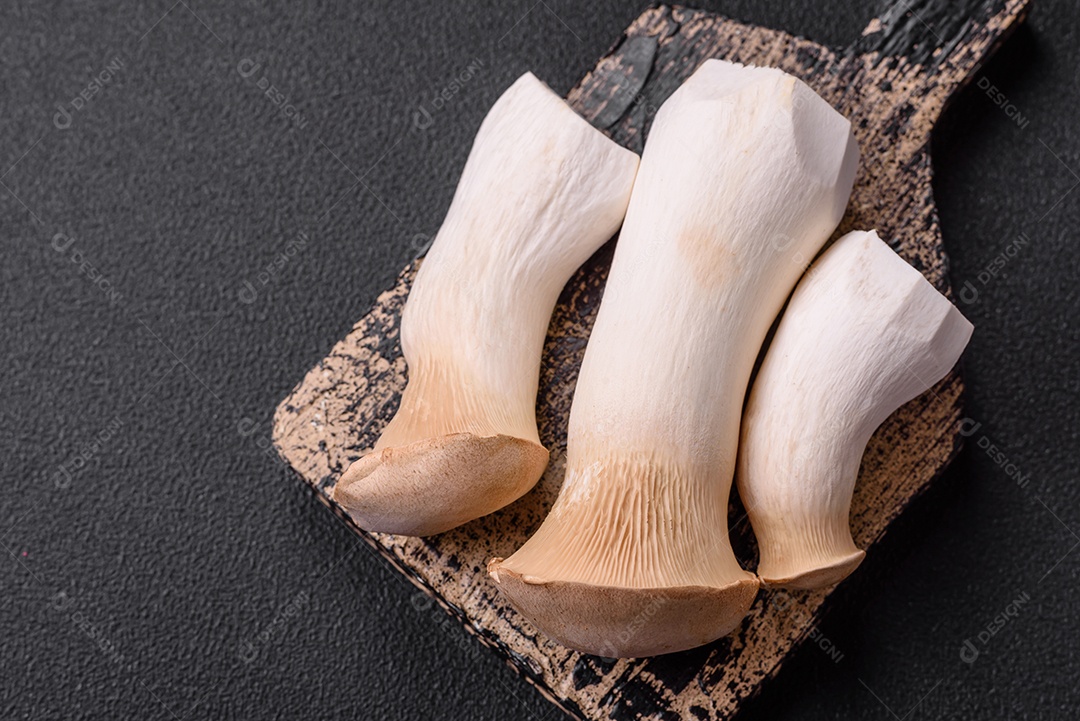 Cogumelos Pleurotus eryngii sobre um fundo escuro de concreto. Cogumelos comestíveis inteiros crus