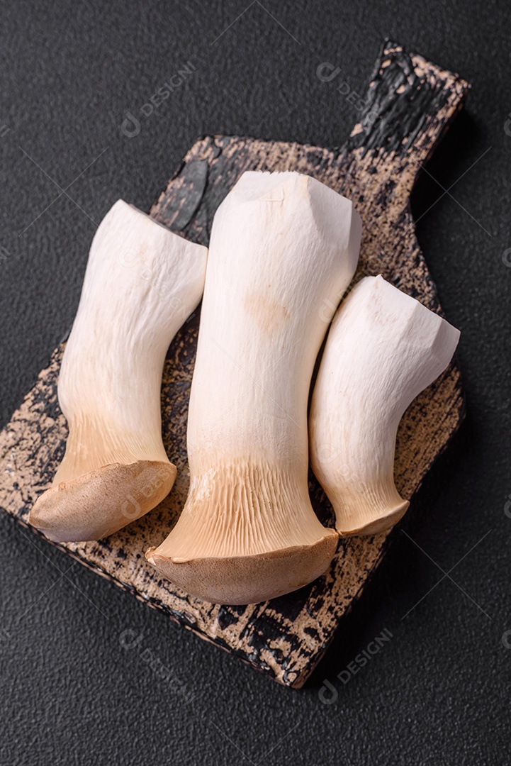 Cogumelos Pleurotus eryngii sobre um fundo escuro de concreto. Cogumelos comestíveis inteiros crus