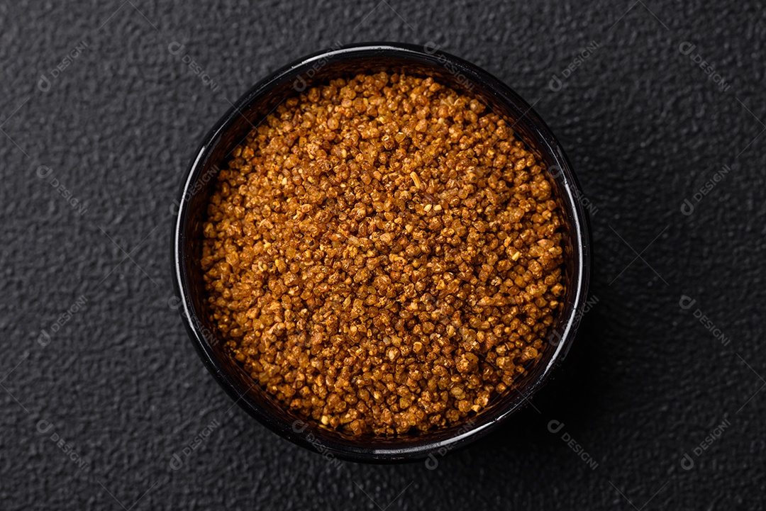 Cristais de sal marrom Svan com especiarias em uma tigela preta sobre um fundo escuro de concreto