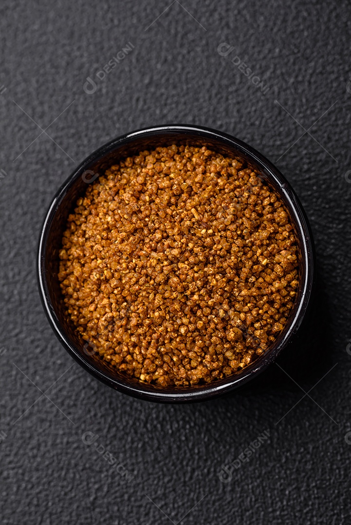 Cristais de sal marrom Svan com especiarias em uma tigela preta sobre um fundo escuro de concreto