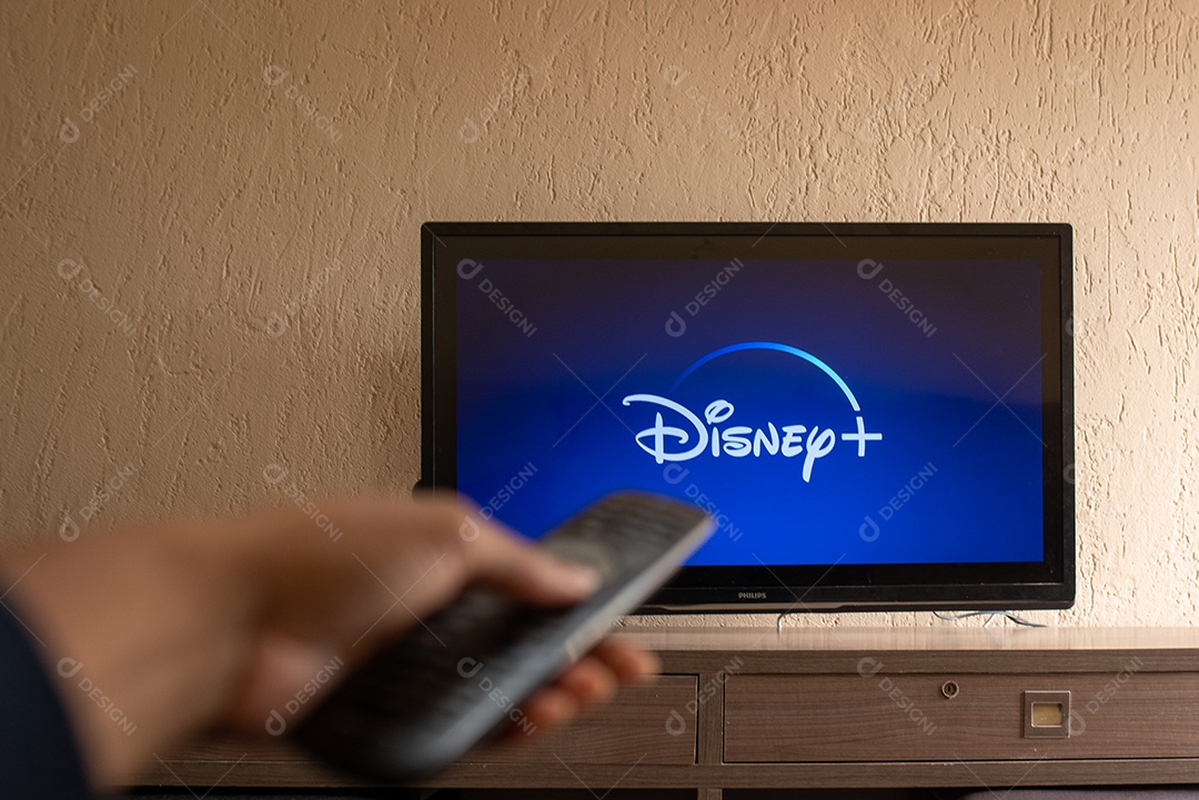Mão com controle ligando tv na Disney+ para assistir