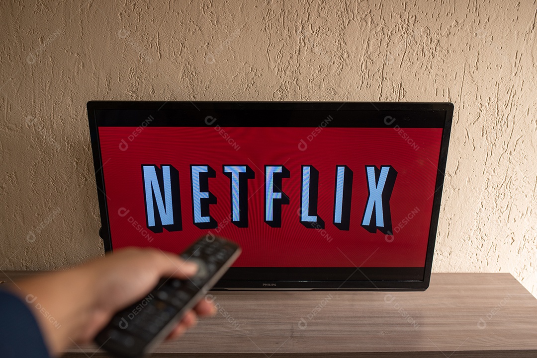 Mão com controle da tv de tela plana exibindo o logotipo da Netflix