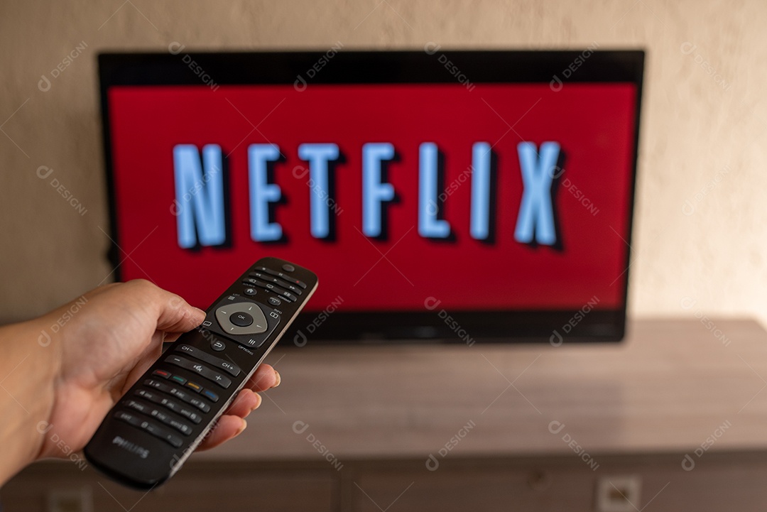 Mão com controle da tv de tela plana exibindo o logotipo da Netflix