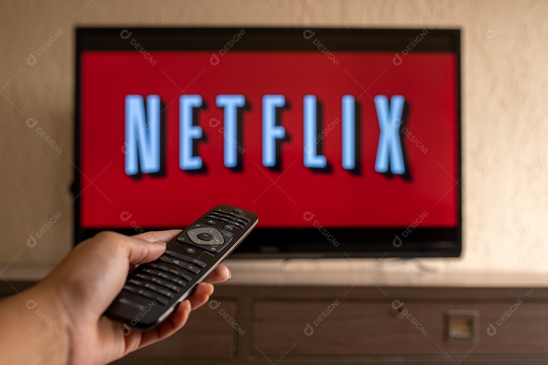Mão com controle da tv de tela plana exibindo o logotipo da Netflix