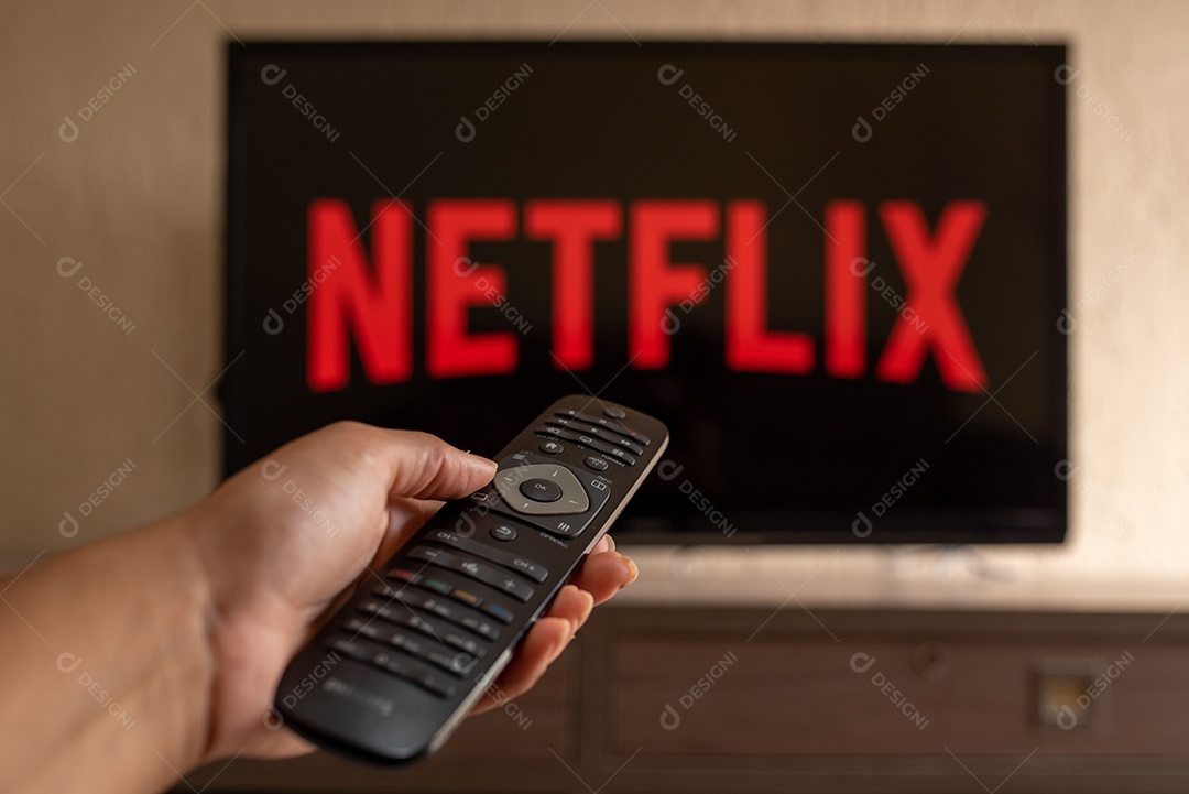 Mão com controle da tv de tela plana exibindo o logotipo da Netflix