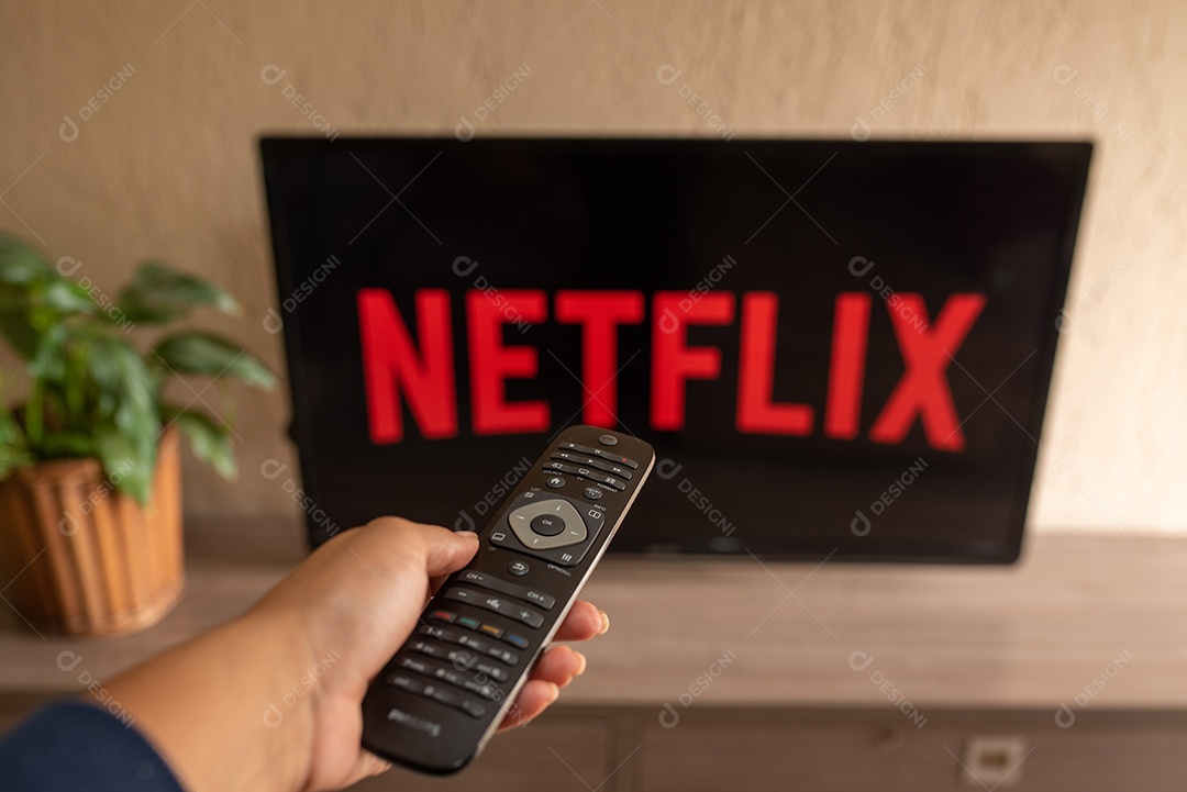 Mão com controle da tv de tela plana exibindo o logotipo da Netflix