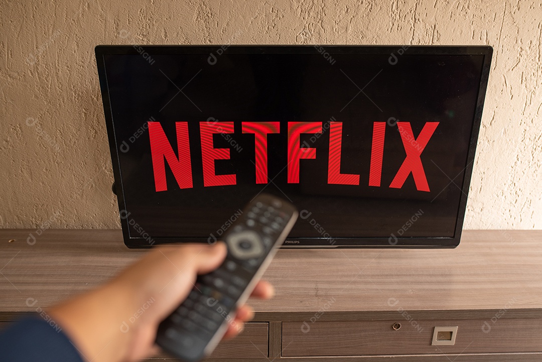 Mão com controle da tv de tela plana exibindo o logotipo da Netflix