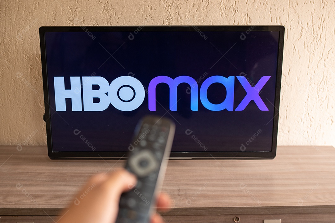 Mão com controle da tv de tela plana exibindo o logotipo da HBO Max