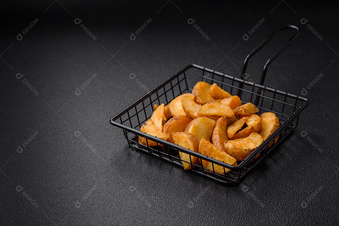 Deliciosas fatias de batata frita crocante com sal, especiarias e ervas sobre um fundo escuro de concreto