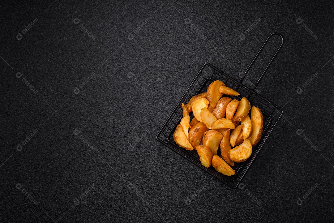 Deliciosas fatias de batata frita crocante com sal, especiarias e ervas sobre um fundo escuro de concreto