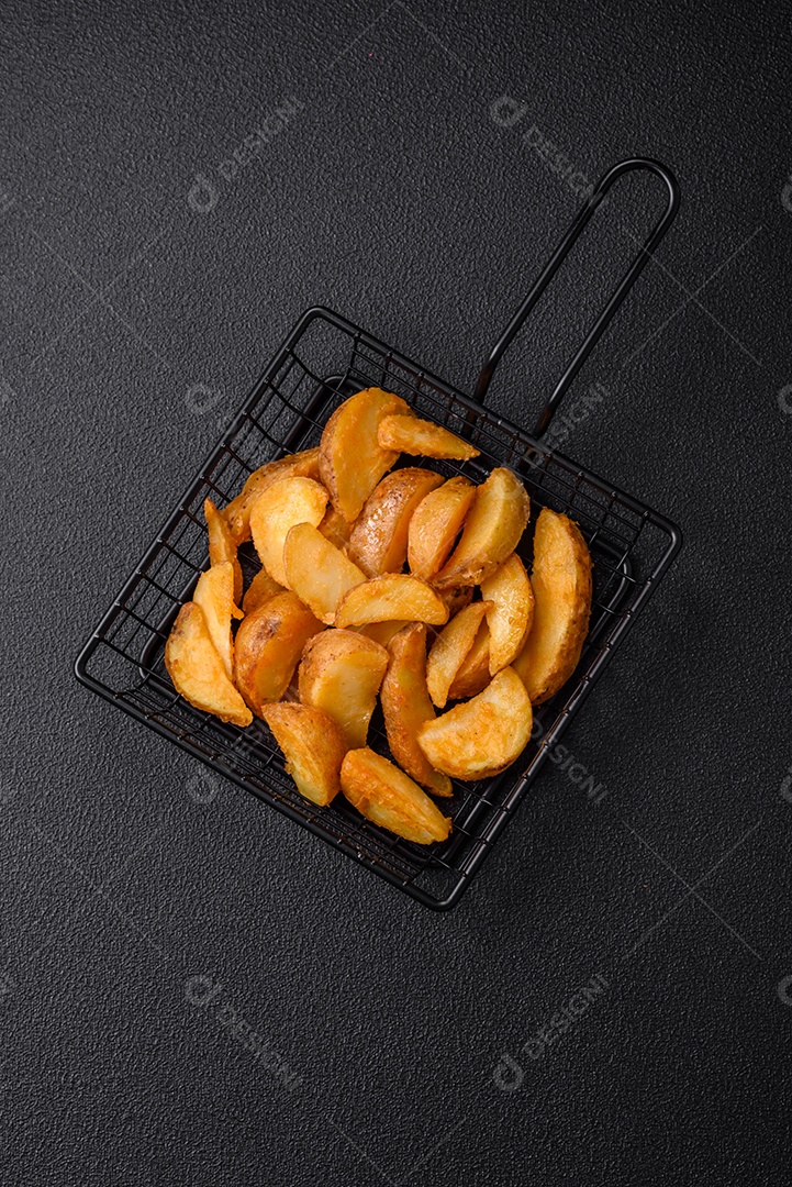 Deliciosas fatias de batata frita crocante com sal, especiarias e ervas sobre um fundo escuro de concreto