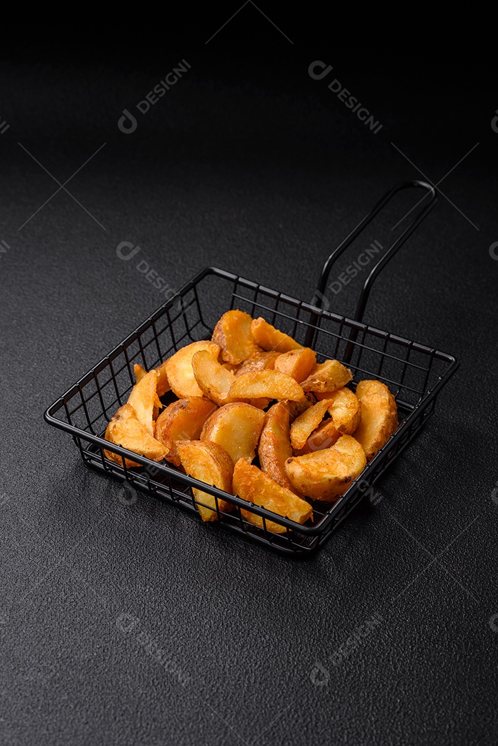 Deliciosas fatias de batata frita crocante com sal, especiarias e ervas sobre um fundo escuro de concreto