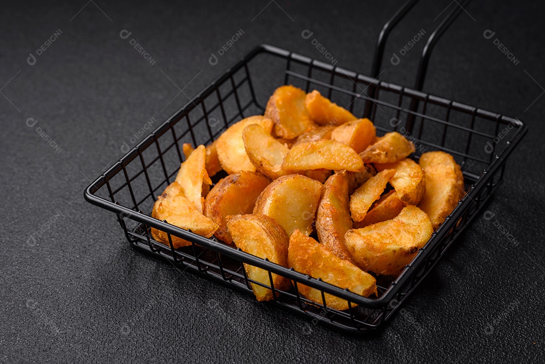 Deliciosas fatias de batata frita crocante com sal, especiarias e ervas sobre um fundo escuro de concreto