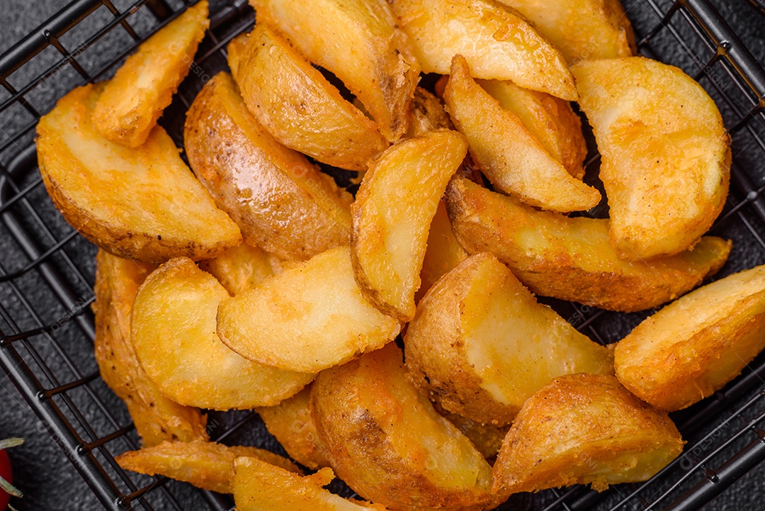 Deliciosas fatias de batata frita crocante com sal, especiarias e ervas sobre um fundo escuro de concreto