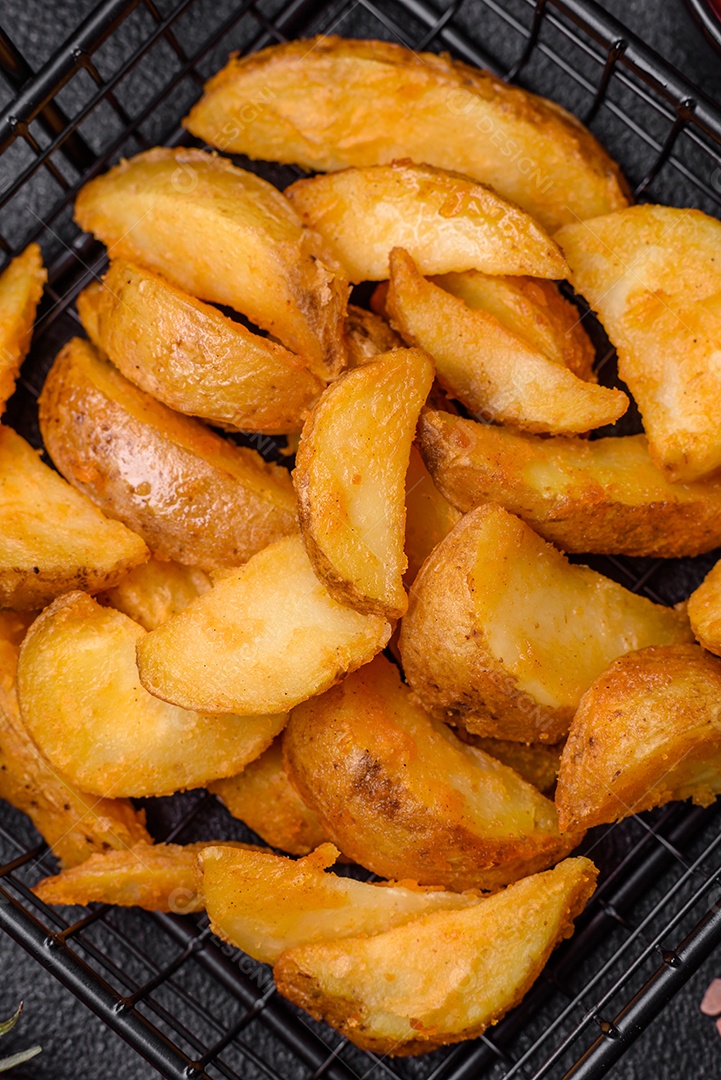 Deliciosas fatias de batata frita crocante com sal, especiarias e ervas sobre um fundo escuro de concreto