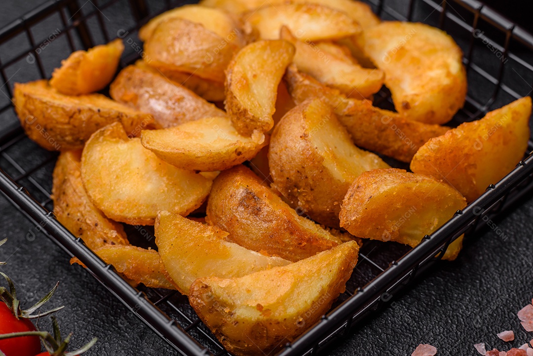Deliciosas fatias de batata frita crocante com sal, especiarias e ervas sobre um fundo escuro de concreto