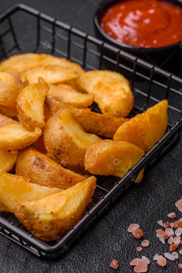 Deliciosas fatias de batata frita crocante com sal, especiarias e ervas sobre um fundo escuro de concreto