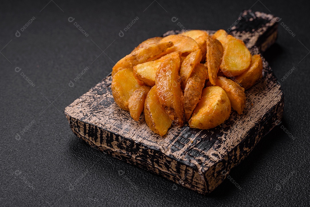 Deliciosas fatias de batata frita crocante com sal, especiarias e ervas sobre um fundo escuro de concreto