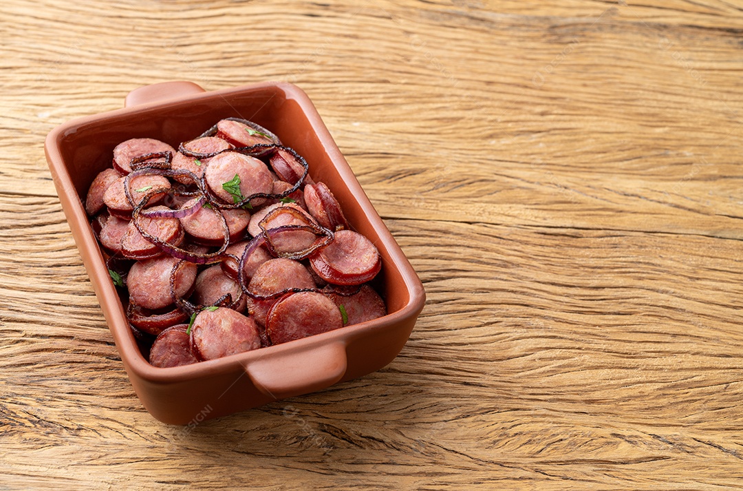 Porção de linguiça calabresa grelhada com cebola sobre mesa de madeira com espaço de cópia.