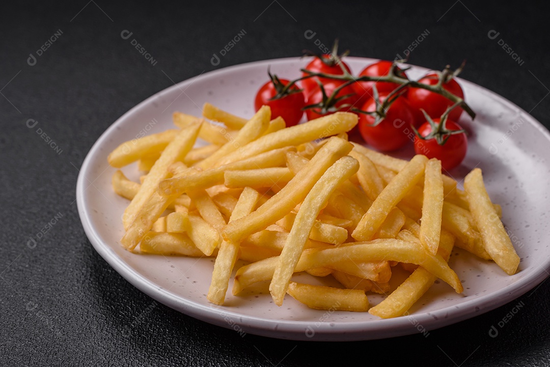Frescas e deliciosas batatas fritas crocantes com sal e especiarias sobre um fundo escuro de concreto