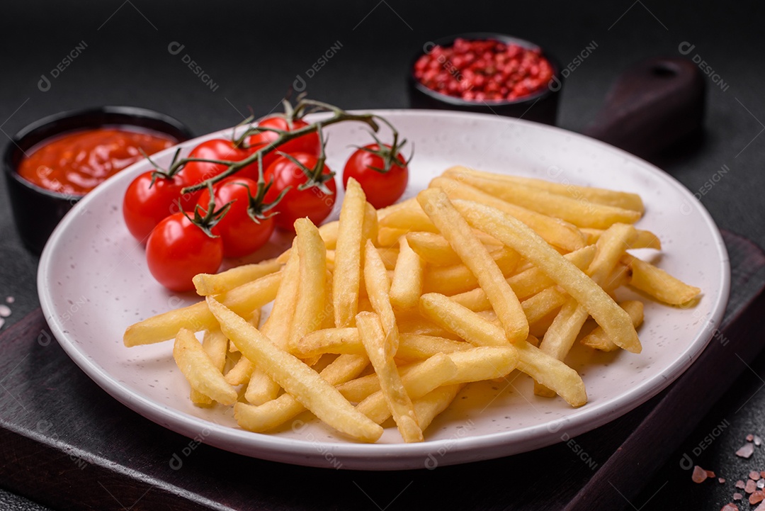 Frescas e deliciosas batatas fritas crocantes com sal e especiarias sobre um fundo escuro de concreto