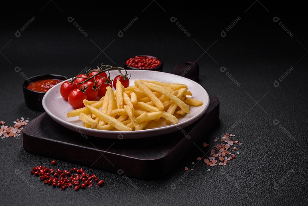 Frescas e deliciosas batatas fritas crocantes com sal e especiarias sobre um fundo escuro de concreto