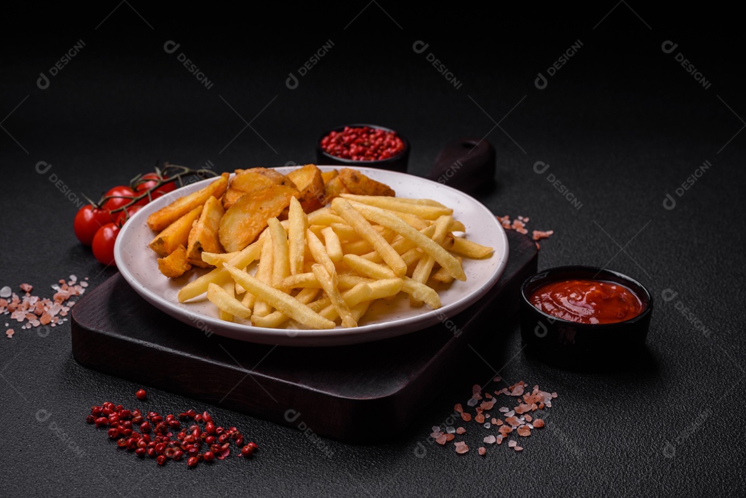 Frescas e deliciosas batatas fritas crocantes com sal e especiarias sobre um fundo escuro de concreto