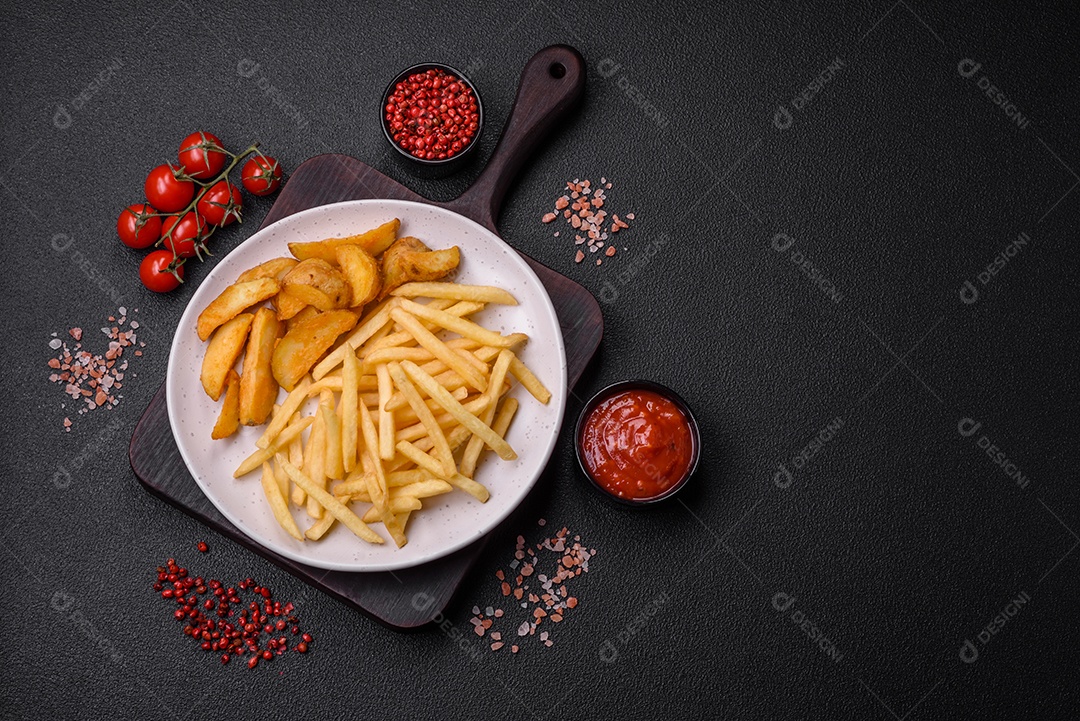 Frescas e deliciosas batatas fritas crocantes com sal e especiarias sobre um fundo escuro de concreto