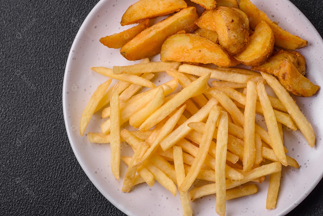 Deliciosas fatias de batata frita crocante com sal, especiarias e ervas sobre um fundo escuro de concreto