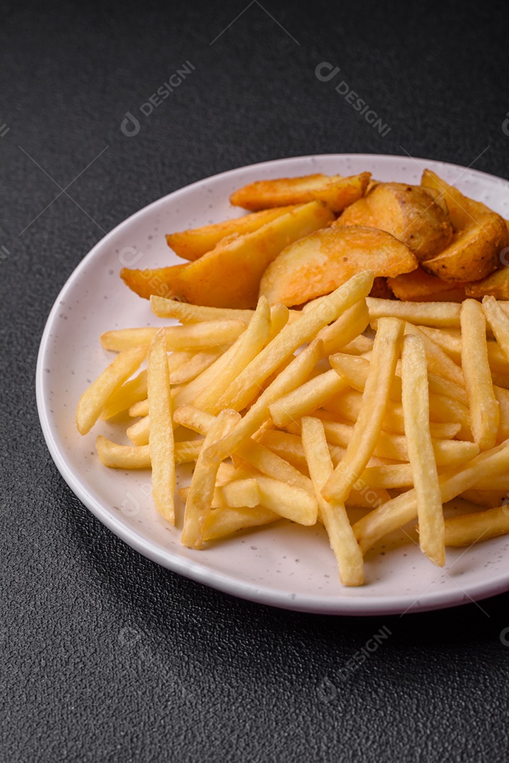Deliciosas fatias de batata frita crocante com sal, especiarias e ervas sobre um fundo escuro de concreto