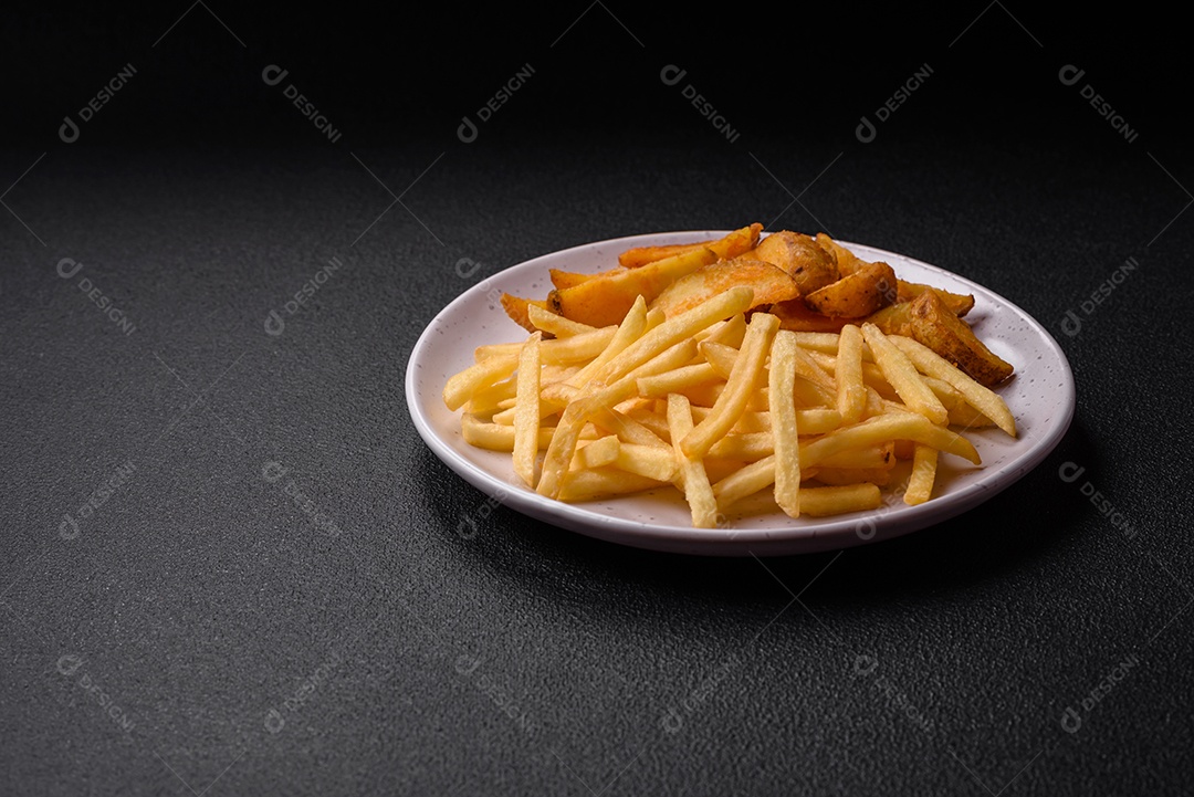Deliciosas fatias de batata frita crocante com sal, especiarias e ervas sobre um fundo escuro de concreto