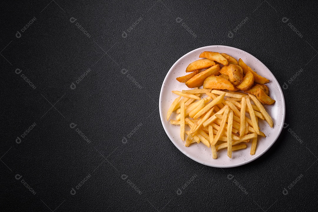 Deliciosas fatias de batata frita crocante com sal, especiarias e ervas sobre um fundo escuro de concreto